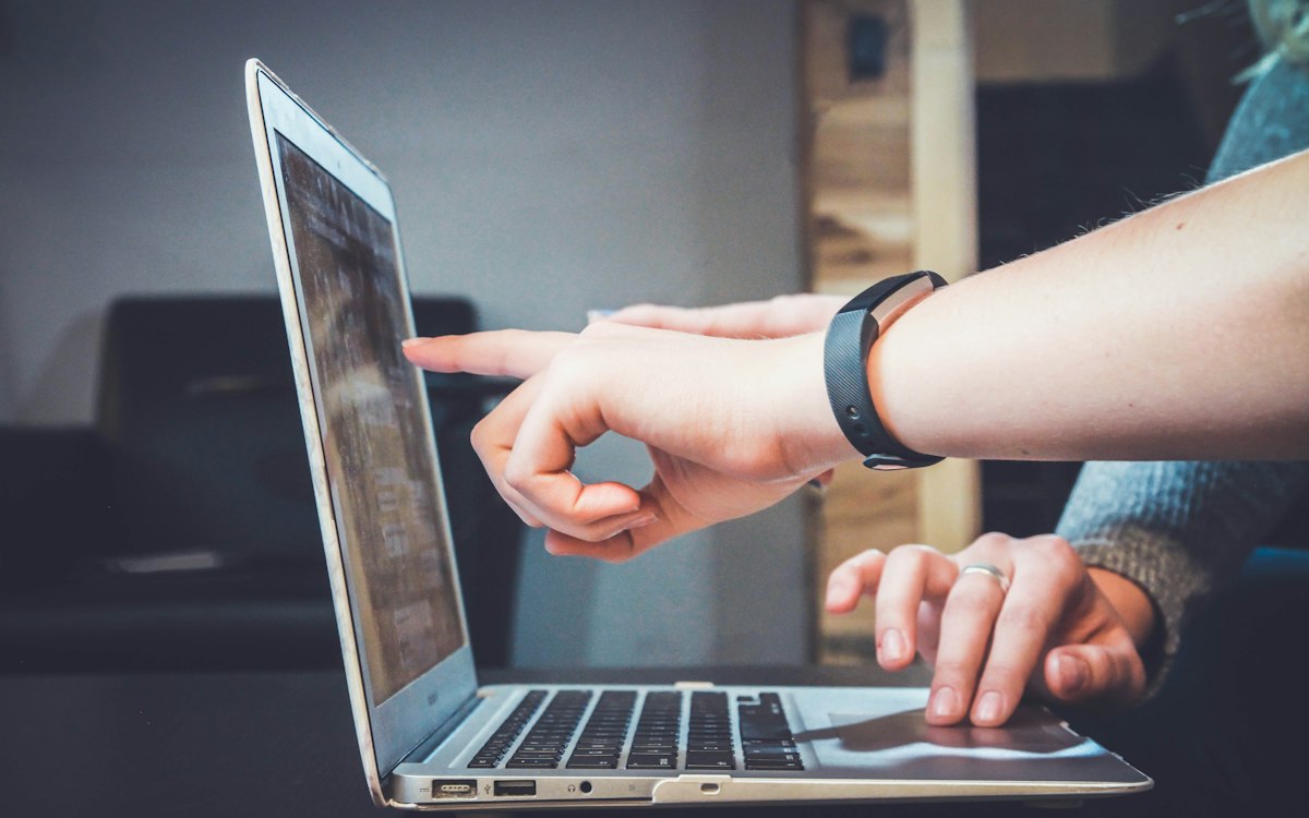 A hand pointing to a laptop screen during a conversation.